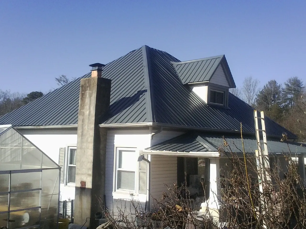 Dark blue standing seam metal roof on a white farmhouse with dormer — Slate & Tile Roof Repair by Roofing Brothers in Wellsville
