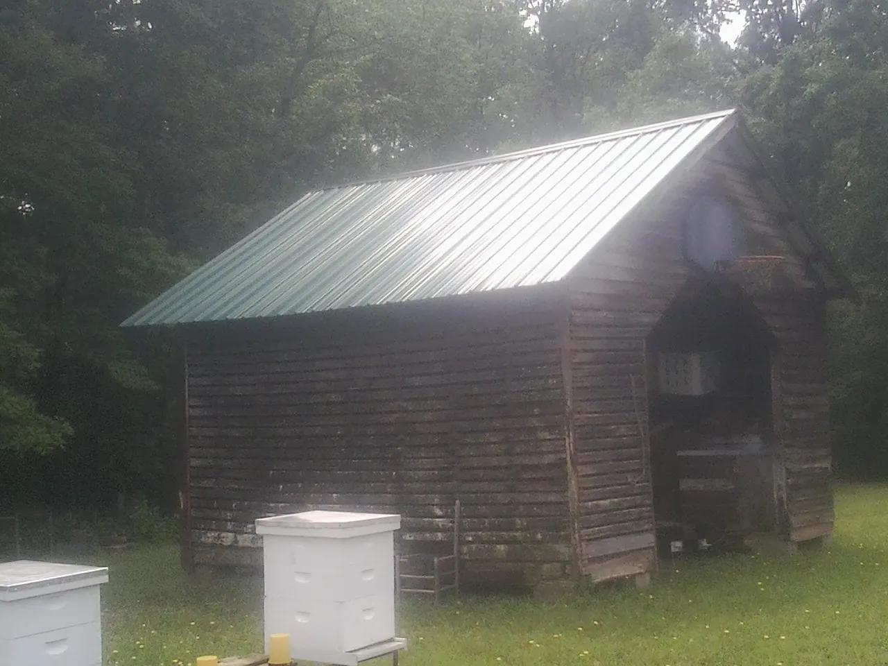 Green metal roof on a weathered barn beside stacked beehives in Wellsville