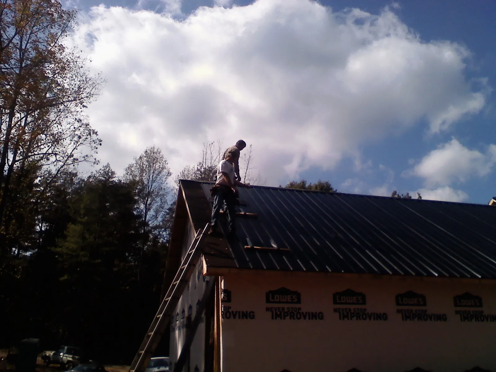Roofer fastening dark metal panels high against a cloudy sky, from a Roof Inspection job in Wellsville